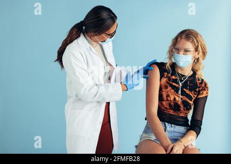 Ärztin, die junge Frau impft. Gesundheitshelfer und Patient tragen Gesichtsmasken während der Impfung. Impfung während der Covid-19-Pandemie Stockfoto