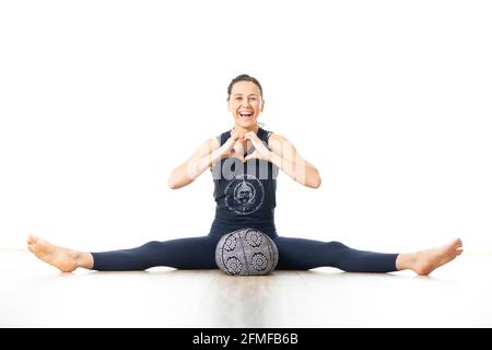 Erholendes Yoga mit einem Aufpolster. Junge sportliche weibliche Yogalehrerin im leuchtend weißen Yogastudio, auf Polsterkissen liegend, dehnend, smilling Stockfoto