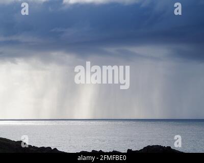 Bei Regen auf dem Meer schweben dramatische dunkelblaue graue Regenwolken über dem Pazifischen Ozean mit Sonnenlicht, das von hinten scheint, glitzerndes silbernes Wasser, Horizont Stockfoto