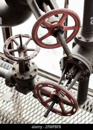 Drei rote Industrieventile aus Metall mit Schwungrad auf Chemierohr mit Öldichtungen, Schrauben und Muttern in der Nähe. Details der petrochemischen Unternehmen, Chemie Stockfoto