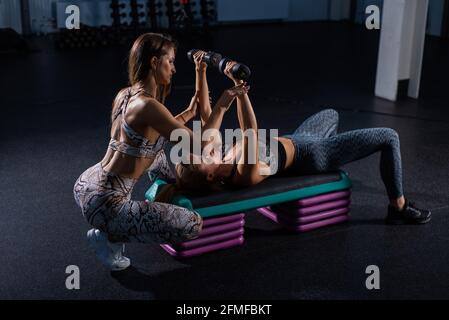 Weibliche Fitnesstrainerin führt persönliches Training durch. Junge attraktive Frau dabei Bankdrücken liegend auf der Plattform mit Hanteln. Mädchen trainiert mit Stockfoto