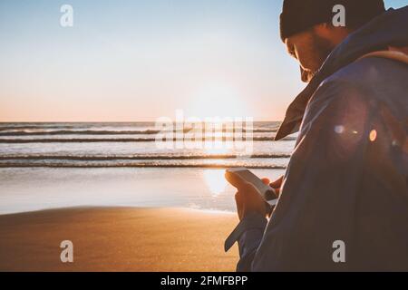 Mann mit Smartphone-Anwendung online zu Fuß am Strand moderne Technologie Influencer Blogger Lifestyle gps Navigation aktiv Urlaub im Freien Stockfoto