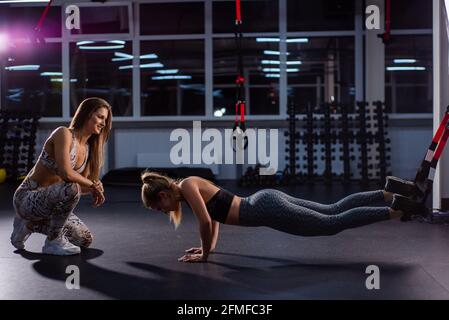 Weibliche Fitnesstrainerin führt persönliches Training durch. Junge attraktive Frau Push-ups mit TPX-Schlaufen an ihren Beinen. Das Mädchen ist mit einem Trainer verlobt Stockfoto