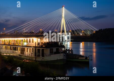 Stadt Warschau in Polen bei Nacht, Boot mit Restaurant-Café auf der Weichsel und beleuchtete Swietokrzyski-Brücke (Heilige Kreuz-Brücke). Stockfoto