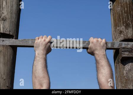 Starke männliche Hände fest greifende Holzleiter Schritt, hängend, blauer Himmel im Hintergrund Stockfoto