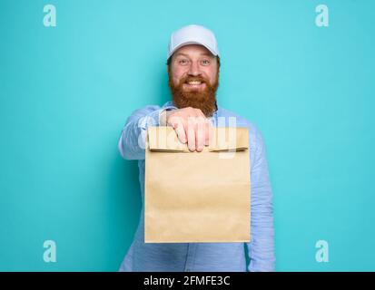 Deliveryman mit wunderten Ausdruck bereit, Beutel mit Lebensmitteln zu liefern. Cyan Hintergrund. Stockfoto