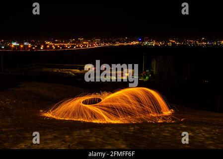 Großes rundes brennendes Feuerwerk funkelt aus der brennenden Stahlwolle. Die Stadt leuchtet bei Nacht. Stockfoto