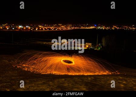 Großes rundes brennendes Feuerwerk funkelt aus der brennenden Stahlwolle. Die Stadt leuchtet bei Nacht. Stockfoto