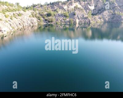 Felsige Ufer des Radon Lake an einem sonnigen Sommermorgen. Luftaufnahme eines alten überfluteten Granitsteinbruchs. Ein malerischer Teich. Stockfoto