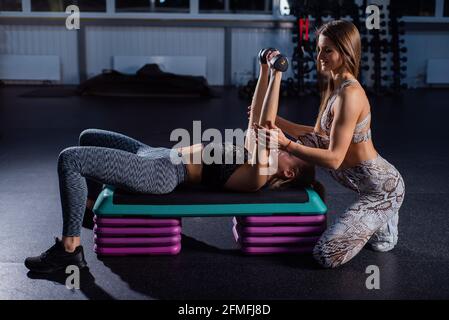 Weibliche Fitnesstrainerin führt persönliches Training durch. Junge attraktive Frau dabei Bankdrücken liegend auf der Plattform mit Hanteln. Mädchen trainiert mit Stockfoto