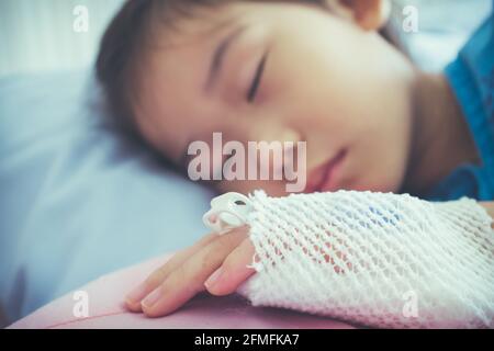 Nahaufnahme der Erkrankung asiatisches Kind im Krankenhaus eingeliefert mit Kochsalzlösung intravenös (IV) zur Hand. Mädchen schläft in komfortabel ausgestatteten Krankenhauszimmer. Gesundheit Stockfoto