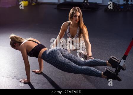 Weibliche Fitnesstrainerin führt persönliches Training durch. Junge attraktive Frau Liegestütze mit Schlaufen auf ihre Beine. Das Mädchen ist mit einem Trainer verlobt Stockfoto