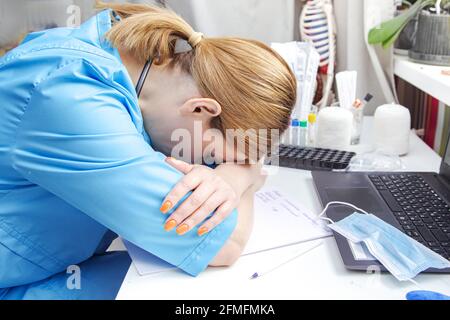 Müde Ärztin mittleren Alters arbeitet an einem Laptop. Arztpraxis, medizinische Geräte. Stockfoto