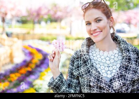 Glückliche junge Rotschopf kaukasische Frau mit toothy Lächeln halten rosa Kirschblütenporträt Stockfoto