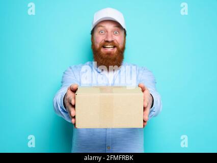 Courier liefert Ihnen gerne einen Karton. Emotionaler Ausdruck. Cyanfarbener Hintergrund Stockfoto