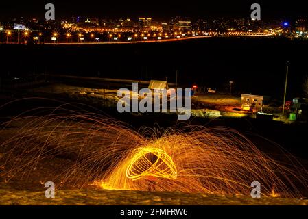 Großes rundes brennendes Feuerwerk funkelt aus der brennenden Stahlwolle. Die Stadt leuchtet bei Nacht. Stockfoto