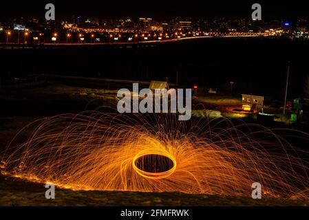 Großes rundes brennendes Feuerwerk funkelt aus der brennenden Stahlwolle. Die Stadt leuchtet bei Nacht. Stockfoto