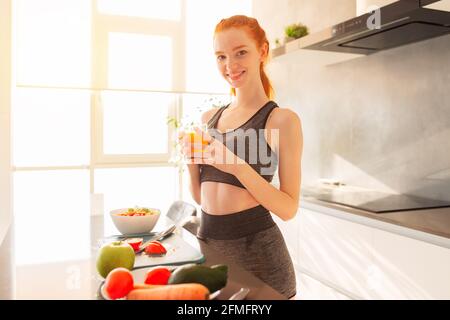 Athletische junge rothaarige Frau in der Küche mit einem Glas Fruchtsaft zentrifugiert Stockfoto
