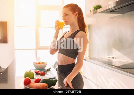 Athletische junge rothaarige Frau in der Küche trinkt ein Glas Fruchtsaft zentrifugiert Stockfoto