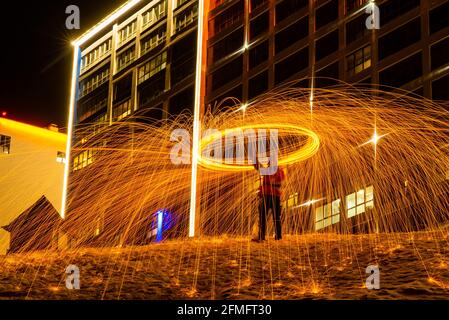 Großes rundes brennendes Feuerwerk funkelt aus der brennenden Stahlwolle. Die Stadt leuchtet bei Nacht. Stockfoto