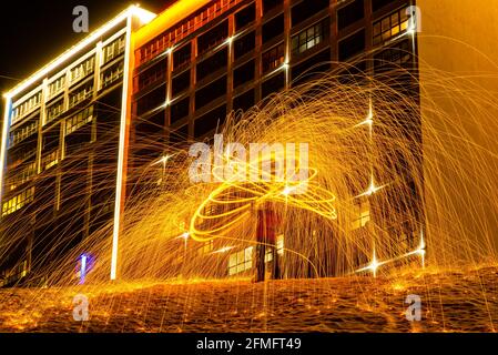 Großes rundes brennendes Feuerwerk funkelt aus der brennenden Stahlwolle. Die Stadt leuchtet bei Nacht. Stockfoto