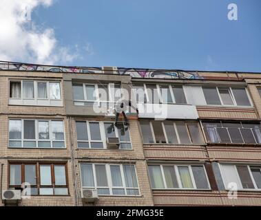 KIEW, UKRAINE - 22. APRIL 2021: Nicht anerkannter Industriekletterer, der an Seilen hängt, renovieren und isolieren die alte Gebäudefassade im Wohnviertel Stockfoto