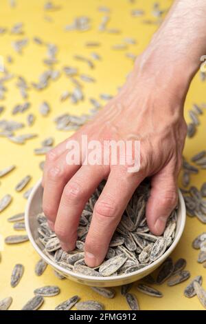 Hand greift ein paar Sonnenblumenkerne aus einer Schüssel Stockfoto