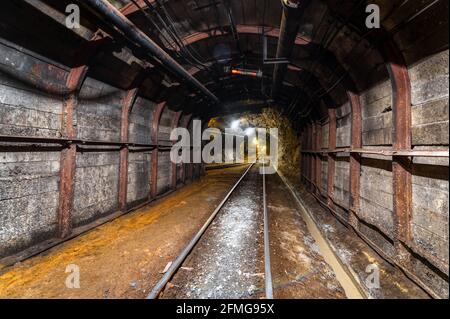 Tunnel des Bergbaus einer unterirdischen Mine. Viele Rohrleitungen an der Decke und Schienenbahn für Trolleys Stockfoto