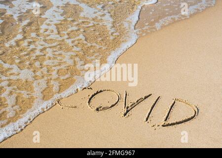 Covid geschrieben auf dem Sand eines Strandes mit Welle waschen das Wort, löschen oder stornieren es während Coronavirus Sommer, Covid frei, sicheren Strand, Impfstoff Stockfoto