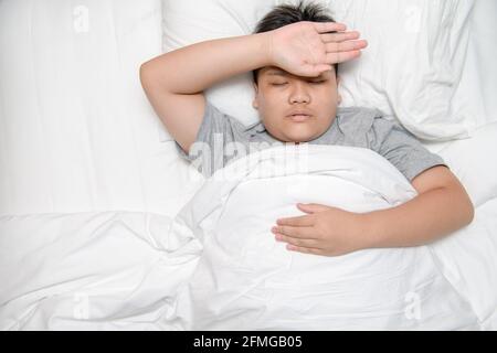 asiatische Kind Junge Krankheit auf dem Bett liegen und legte Hand auf die Stirn, um Temperatur zu überprüfen, Gesundheitskonzept Stockfoto