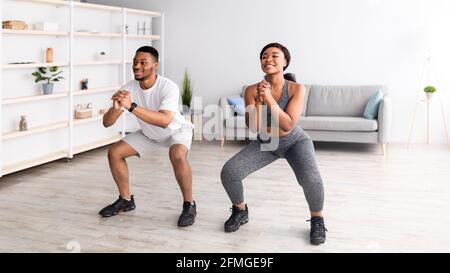 Krafttraining Konzept. Fit schwarze Frau und ihr Freund machen Kniebeugen zusammen zu Hause, Panorama Stockfoto