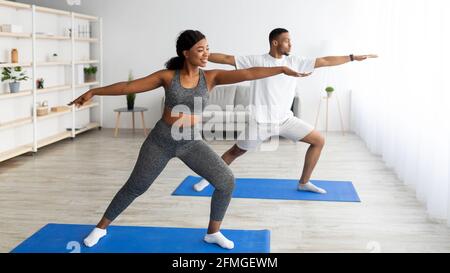 Kraft Yoga Übungen. Fit schwarzes Paar in Kriegerpose, Training auf Sportmatten zu Hause, kopieren Raum Stockfoto