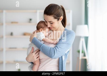 Junge Lächelnde Mutter Hält Ihr Entzückendes Neugeborenes Baby Und Umarmt Ihr Kind Zärtlich Stockfoto
