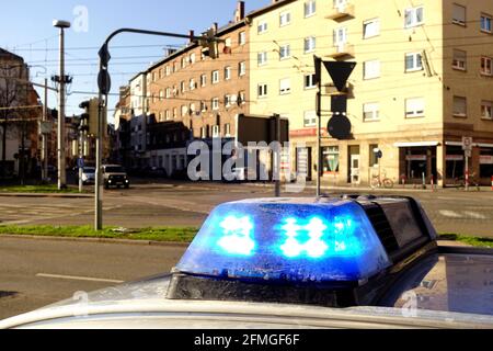 Blaues Blinklicht auf einem Polizeiauto in einer Stadt in Deutschland. Häuser, Autos und Straßen im Hintergrund. Der Fokus liegt auf den blauen Lichtern. Stockfoto