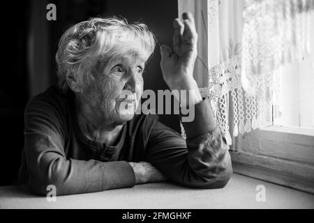 Eine alte Frau, die gestikulierend am Tisch redet. Schwarzweiß-Foto. Stockfoto
