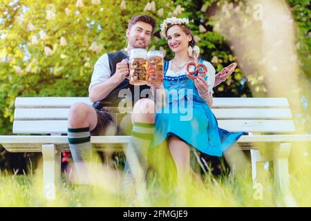 Ein Paar in Bayern sitzt auf der Bank und toasten mit Bier Stockfoto