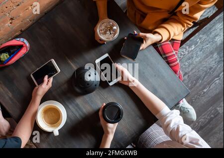 Draufsicht auf weibliche Hände mit Smartphones und Tassen Kaffee auf einem Tisch in einem Café. Drei Freundinnen trinken Kaffee. Stockfoto