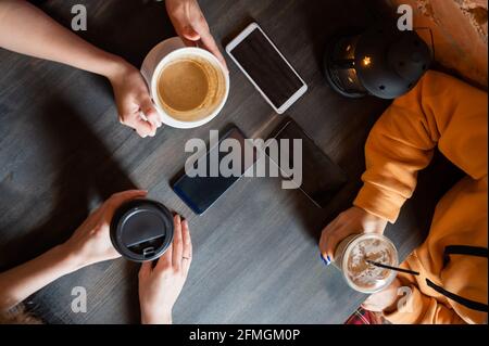 Draufsicht auf weibliche Hände mit Smartphones und Tassen Kaffee auf einem Tisch in einem Café. Drei Freundinnen trinken Kaffee. Stockfoto