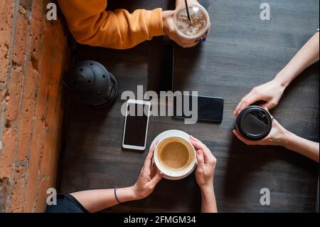 Draufsicht auf weibliche Hände mit Smartphones und Tassen Kaffee auf einem Tisch in einem Café. Drei Freundinnen trinken Kaffee. Stockfoto