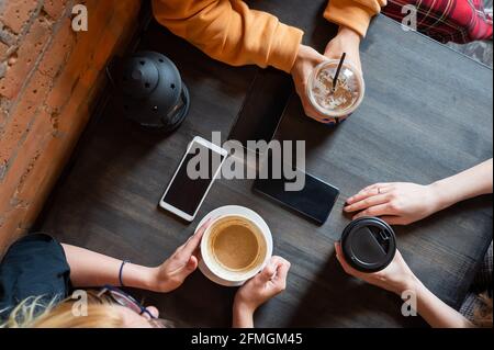 Draufsicht auf weibliche Hände mit Smartphones und Tassen Kaffee auf einem Tisch in einem Café. Drei Freundinnen trinken Kaffee. Stockfoto