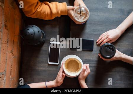 Draufsicht auf weibliche Hände mit Smartphones und Tassen Kaffee auf einem Tisch in einem Café. Drei Freundinnen trinken Kaffee. Stockfoto