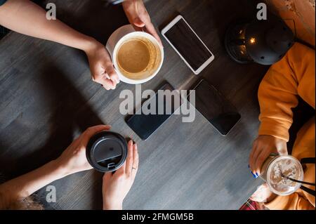 Draufsicht auf weibliche Hände mit Smartphones und Tassen Kaffee auf einem Tisch in einem Café. Drei Freundinnen trinken Kaffee. Stockfoto