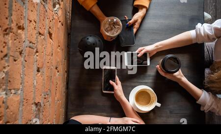 Draufsicht auf weibliche Hände mit Smartphones und Tassen Kaffee auf einem Tisch in einem Café. Drei Freundinnen trinken Kaffee. Stockfoto