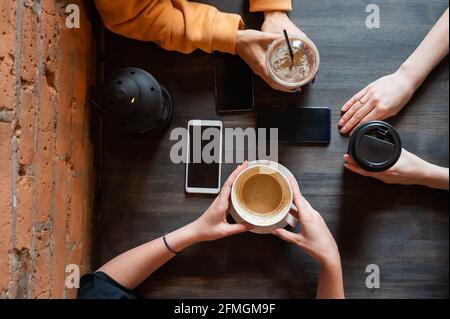 Draufsicht auf weibliche Hände mit Smartphones und Tassen Kaffee auf einem Tisch in einem Café. Drei Freundinnen trinken Kaffee. Stockfoto