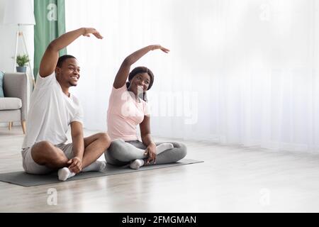 Lächelndes afroamerikanisches Paar sitzt auf einer Fitnessmatte und dehnt sich Stockfoto