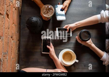 Draufsicht auf weibliche Hände mit Smartphones und Tassen Kaffee auf einem Tisch in einem Café. Drei Freundinnen trinken Kaffee. Stockfoto