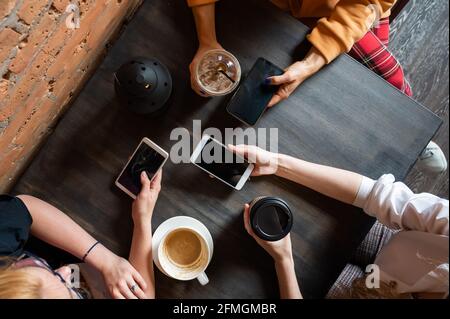 Draufsicht auf weibliche Hände mit Smartphones und Tassen Kaffee auf einem Tisch in einem Café. Drei Freundinnen trinken Kaffee. Stockfoto