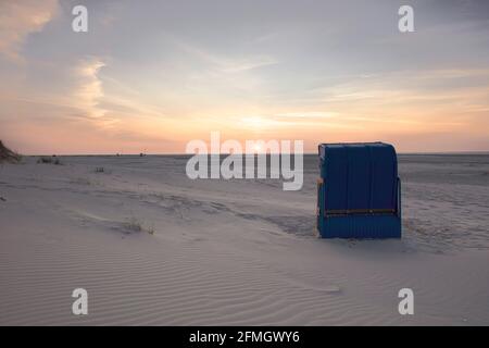 Rückansicht der blauen überdachten Korbliege am leeren Sandstrand bei Sonnenuntergang. Farbenfroher Himmel. Sommerurlaub, Urlaub am Meer Konzept. Stockfoto