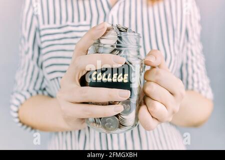 Glas mit Ersparnissen für die Hochschule in Frauenhand. Mädchen in einem gestreiften Hemd hält eine Flasche Münzen. Bildungsfinanzierung. Aufkleber mit Aufschrift. Stockfoto