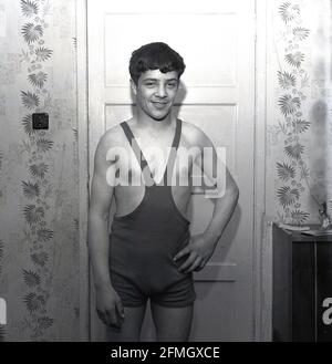 1960s, historisch, ein junger männlicher Wrestler, der in seinem Wrestling Singlet oder einfach Singlet steht, Kelty, Schottland, Großbritannien. Das Singlet ist ein einteiliges, eng anliegender Kostüm oder Sportkit, das den Körper von der Mitte der Brust aus bedeckte, aber die obere Körperhälfte und die Arme ohne Abdeckung frei ließ, Obwohl das einteilige Singlet als die traditionelle Uniform des Sports bekannt ist, wurde es in der Tat erst seit den späten 50er Jahren weit verbreitet, mit Wrestlern vor damals, die Hosen über Leggings mit oder ohne Weste trugen, während des Wettkampfs. Wrestling war eine beliebte Aktivität bei den Highland Games. Stockfoto